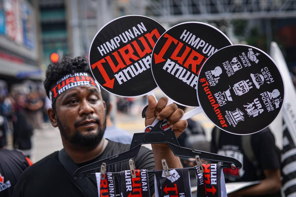 Seorang peserta Himpunan Turun Anwar memegang kipas dan lilitan kepala dengan slogan protes.