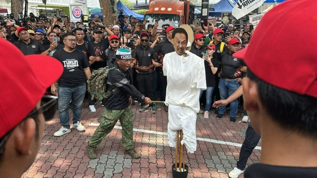 Che'Gu Bard dan demonstran sedang memukul patung menyerupai Anwar Ibrahim.
